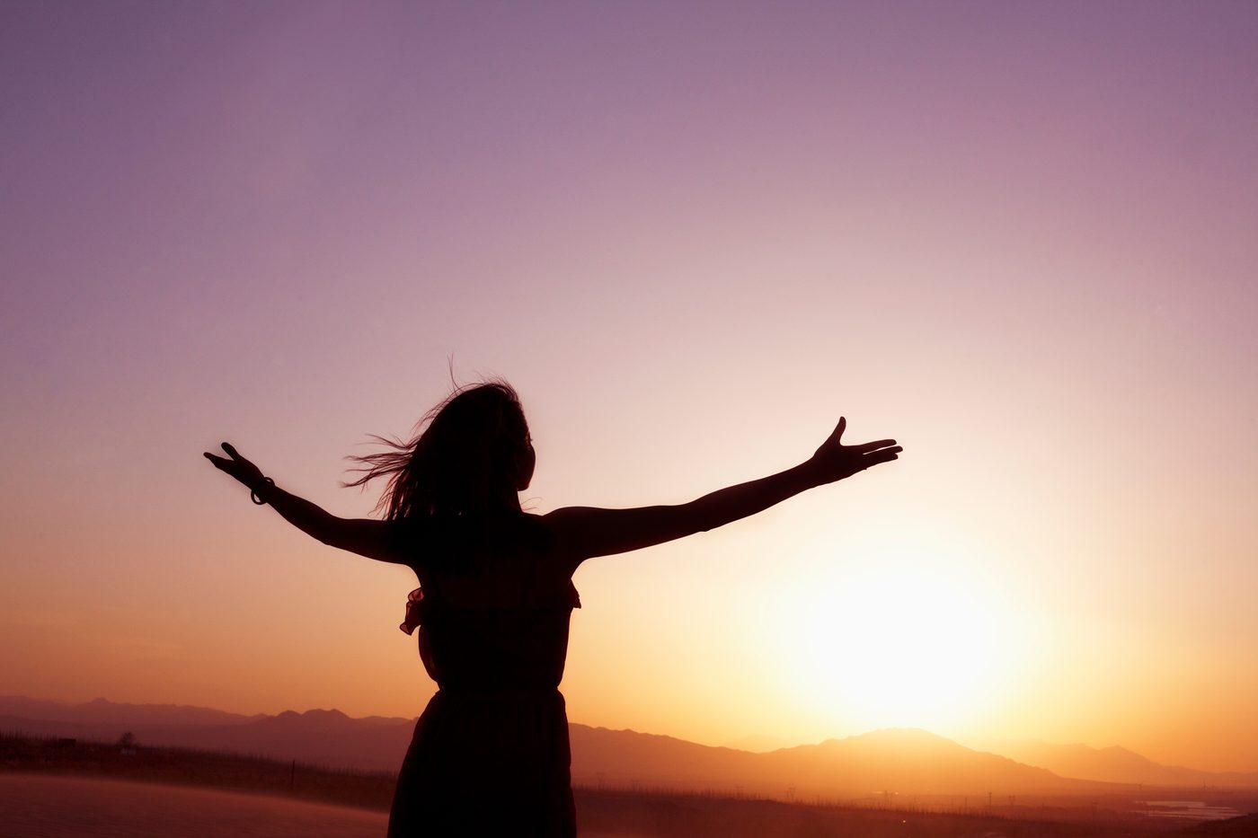 Silhouette with arms outstretched against a sunset sky over the mountains